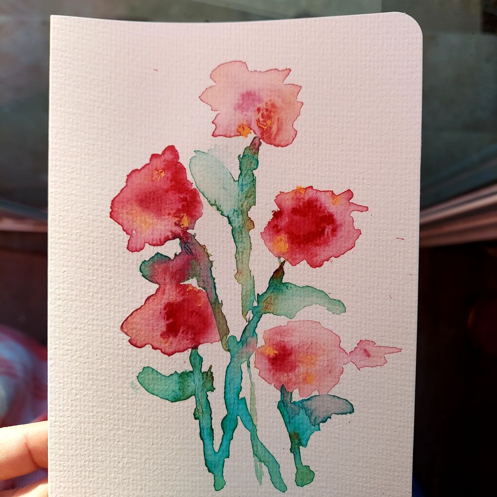 Hand holding watercolor painting of dark pink flowers in a loose, watery style.