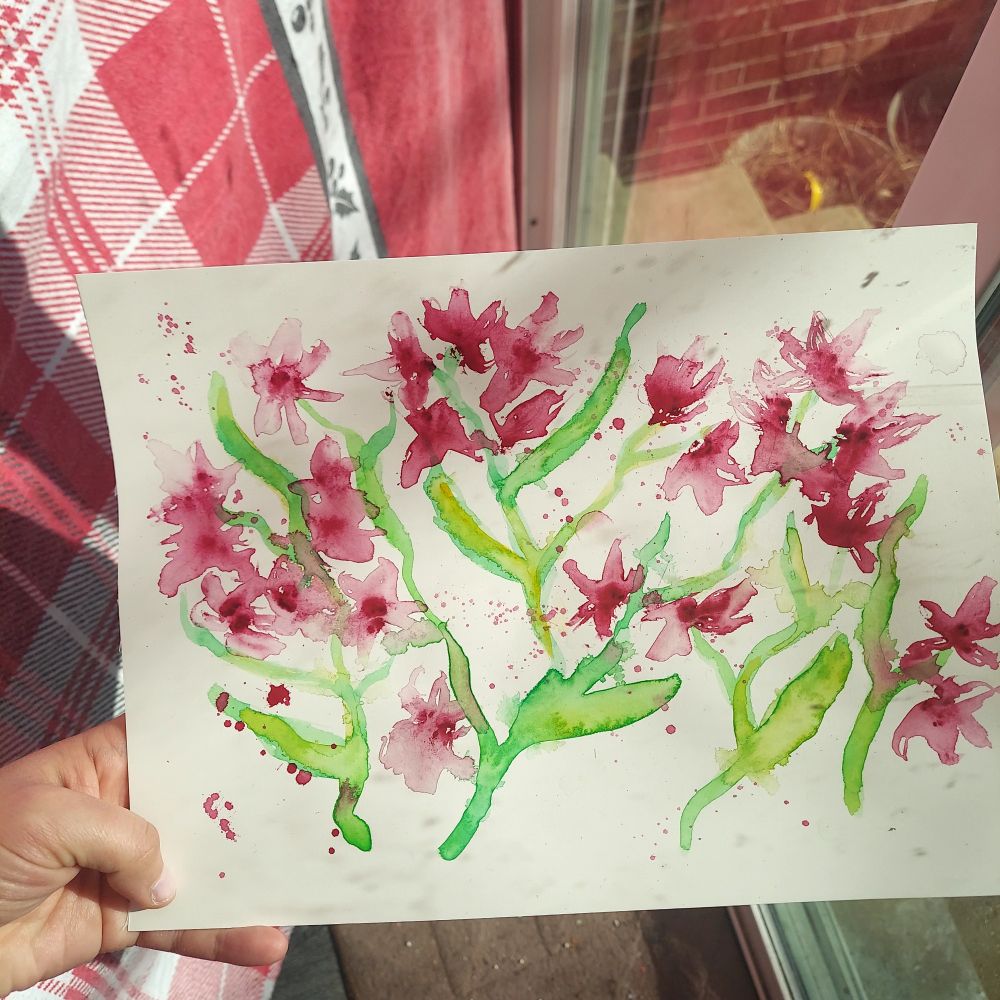 A hand holding paper with dark pink watercolor flowers in a loose, messy style.