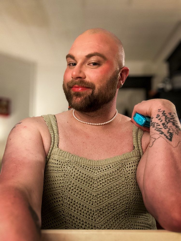 Trans/non-binary person in a green crochet dress, wearing cute makeup posing for a selfie 