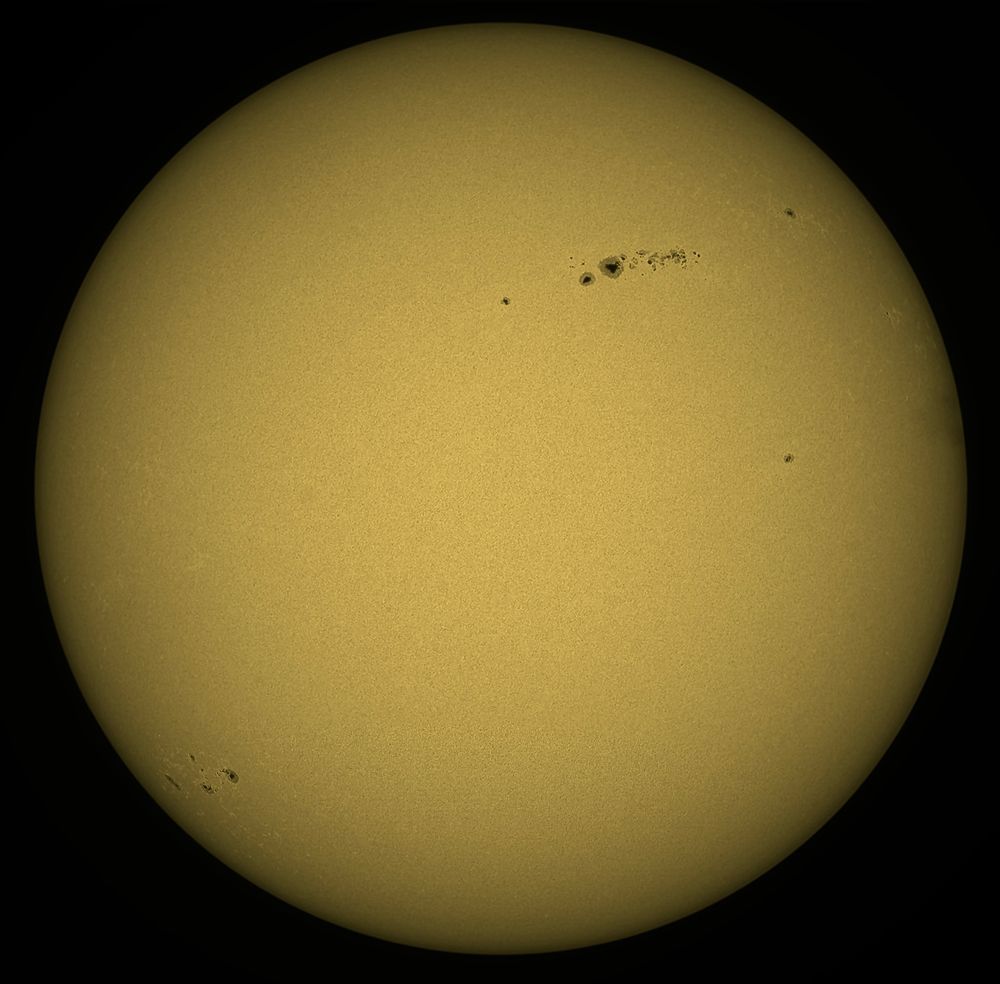 The yellow disk of the Sun showing a few dark sunspots.