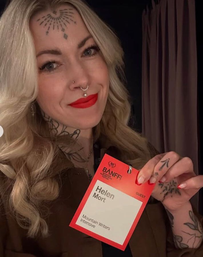 Helen looking at the camera holding up her Banff file festival pass which reads 'Helen Mort. Mountain Writers Intensive'.