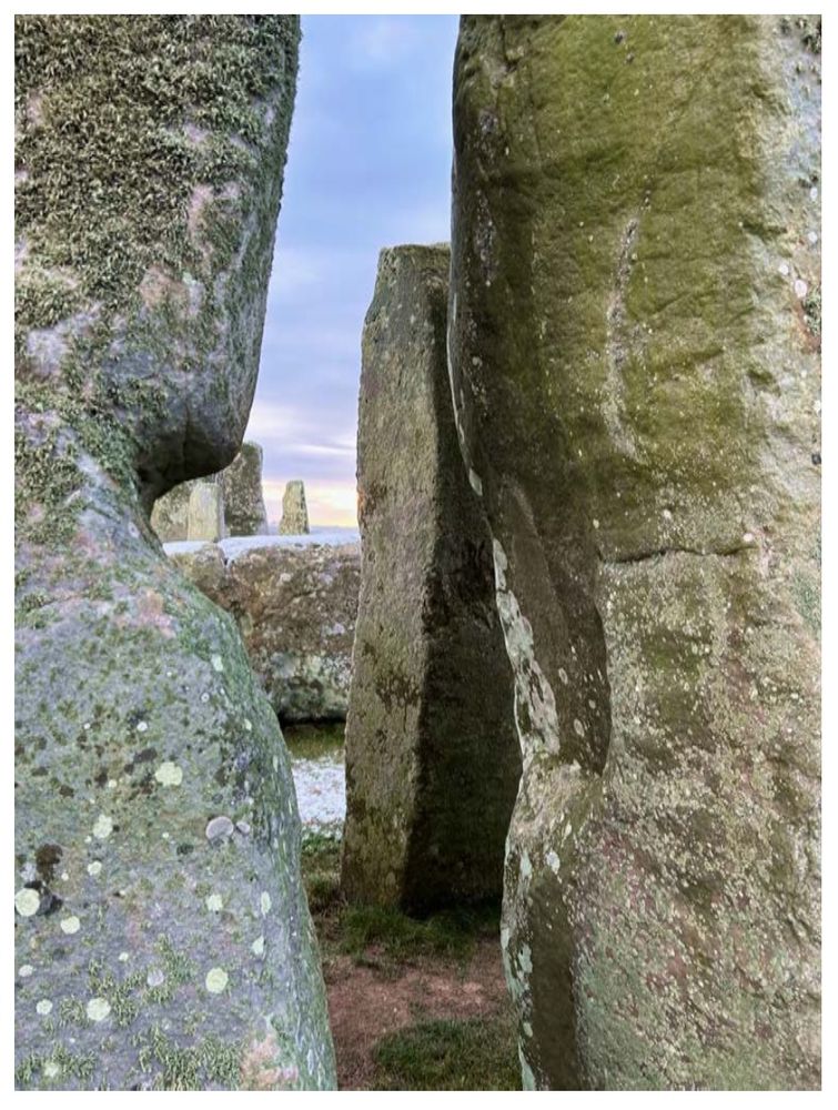 View through stone blocks onto standing stones and blue sky.