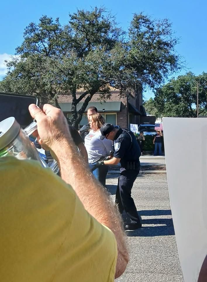 A lady in a trump shirt being handcuffed by a police officer.