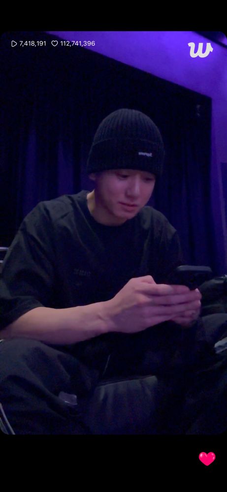 Jungkook in black joggers with white letters on it
Black t shirt and beanie sitting in a dark room looking down on his phone