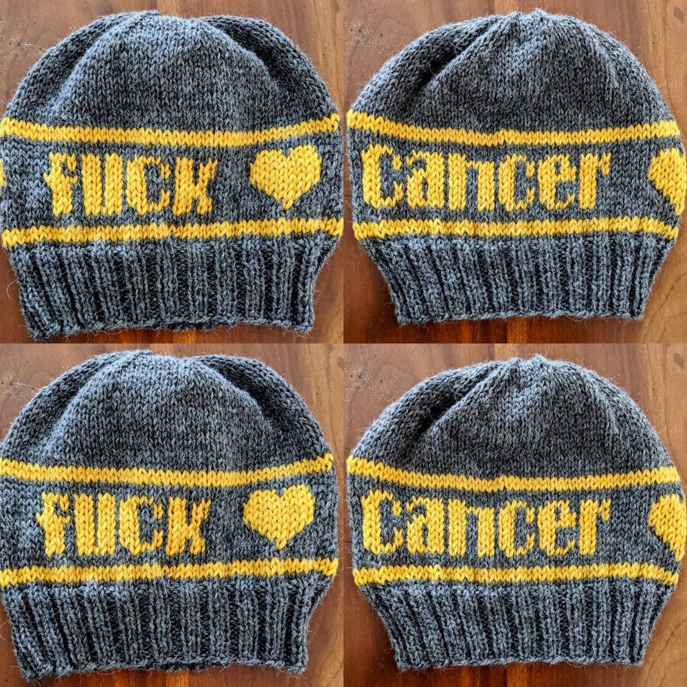 Four hand knit gray hats laid in a grid pattern on a wooden background. The hats have yellow colorwork that says Fuck Cancer and a heart. 