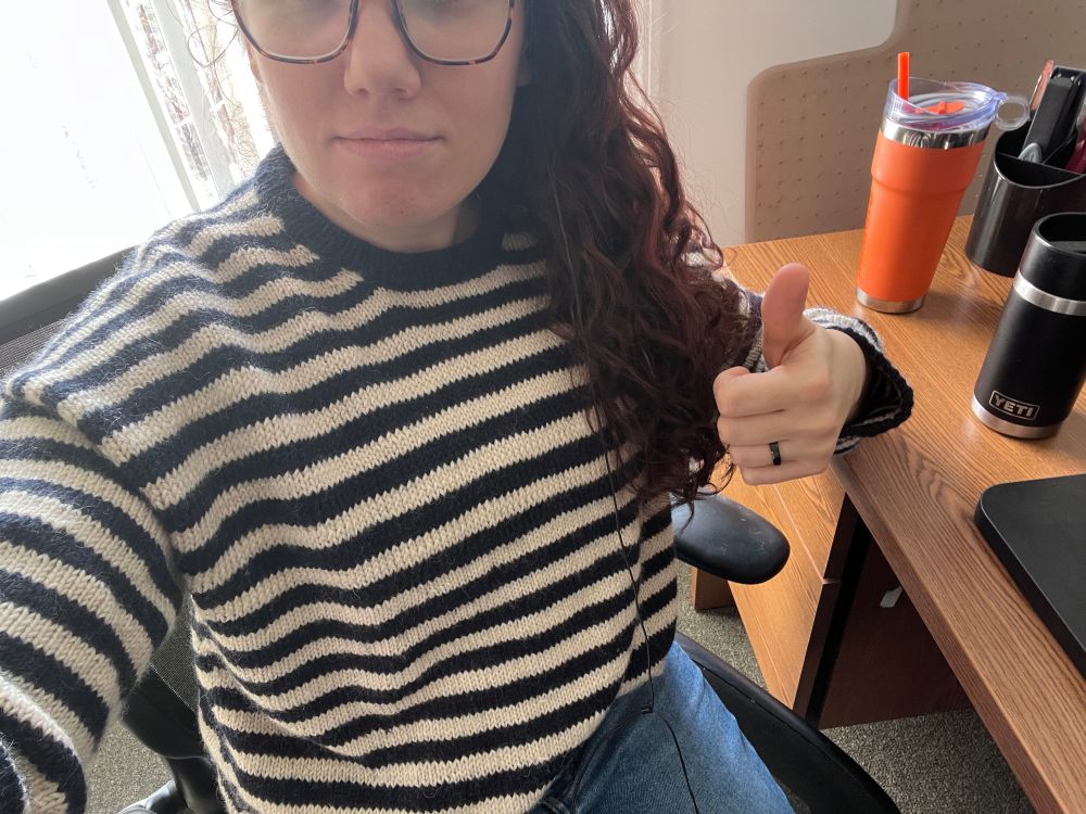 a woman giving a thumbs up and wearing a hand knit Olga sweater by petite knit.
