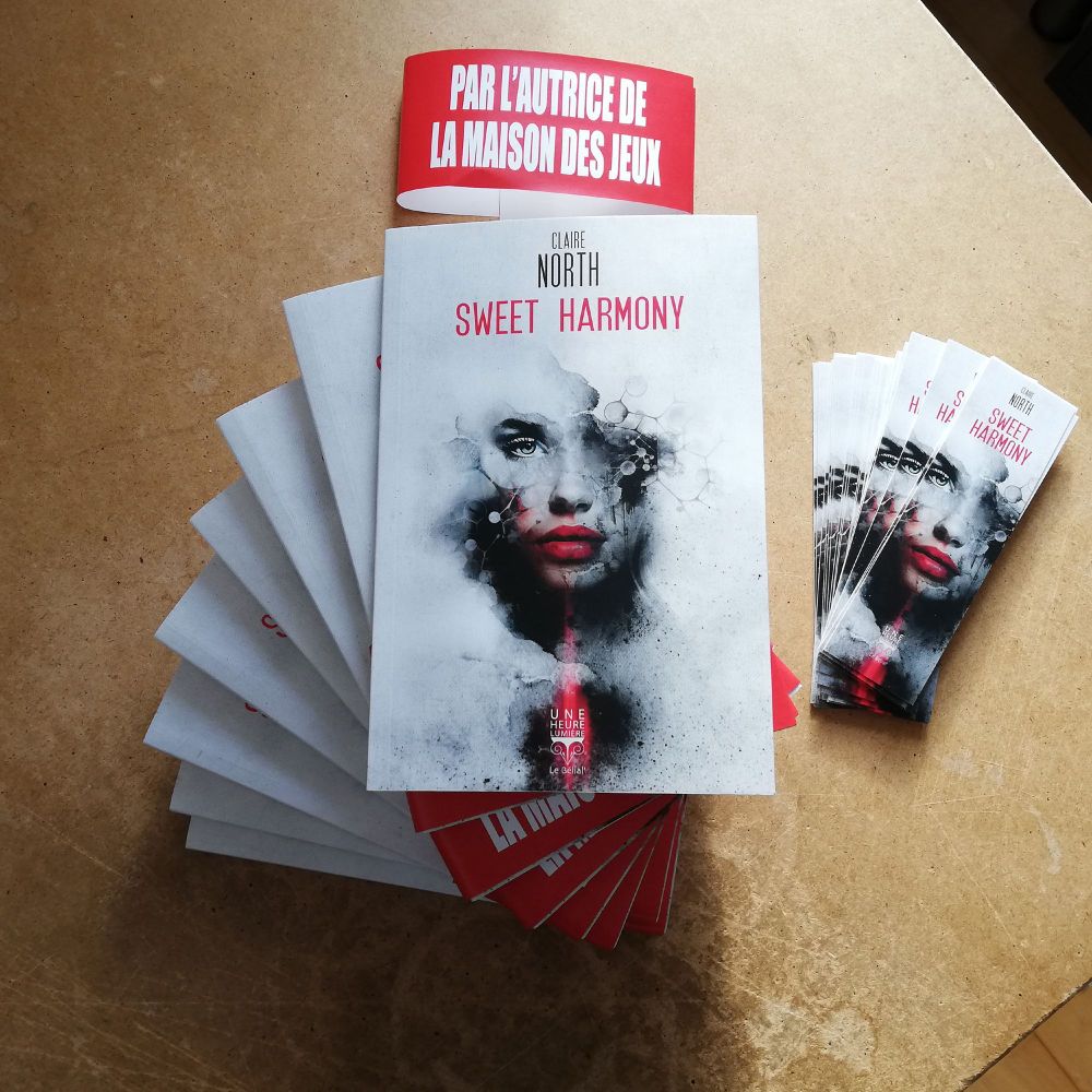 Une pile de volumes du court roman “Sweet Harmony” de Claire North et quelques marque-pages à côté. La couverture représente un visage féminin dans une ambiance informatico-technoïde.