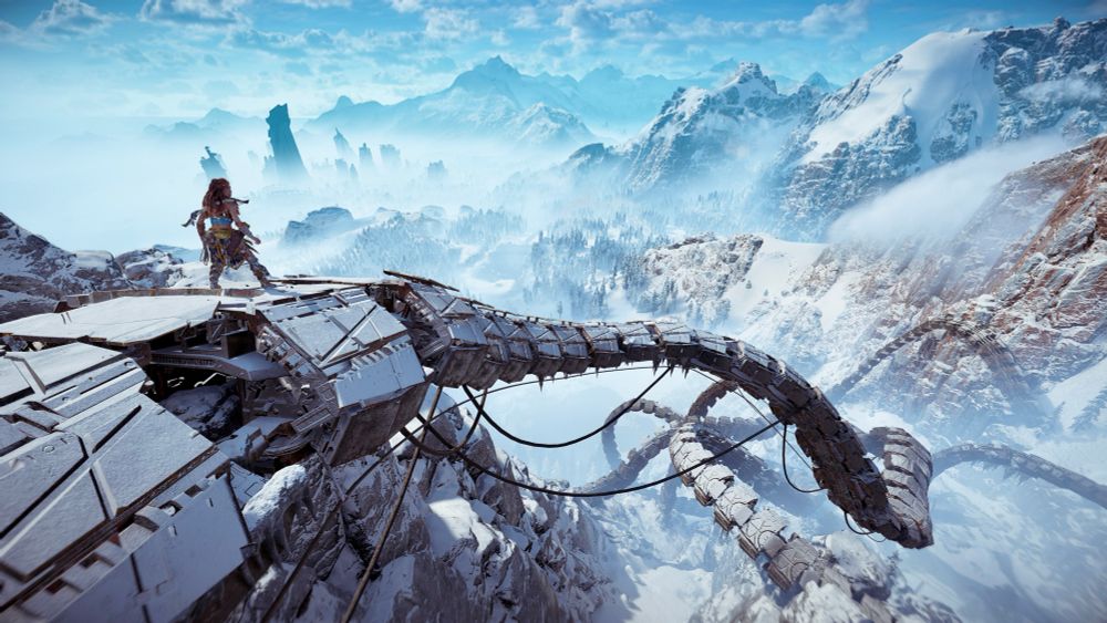 Looking out across an expansive mountain range with rope-like machines connecting the landscape. Aloy is standing atop one of the machines looking out across the scene.