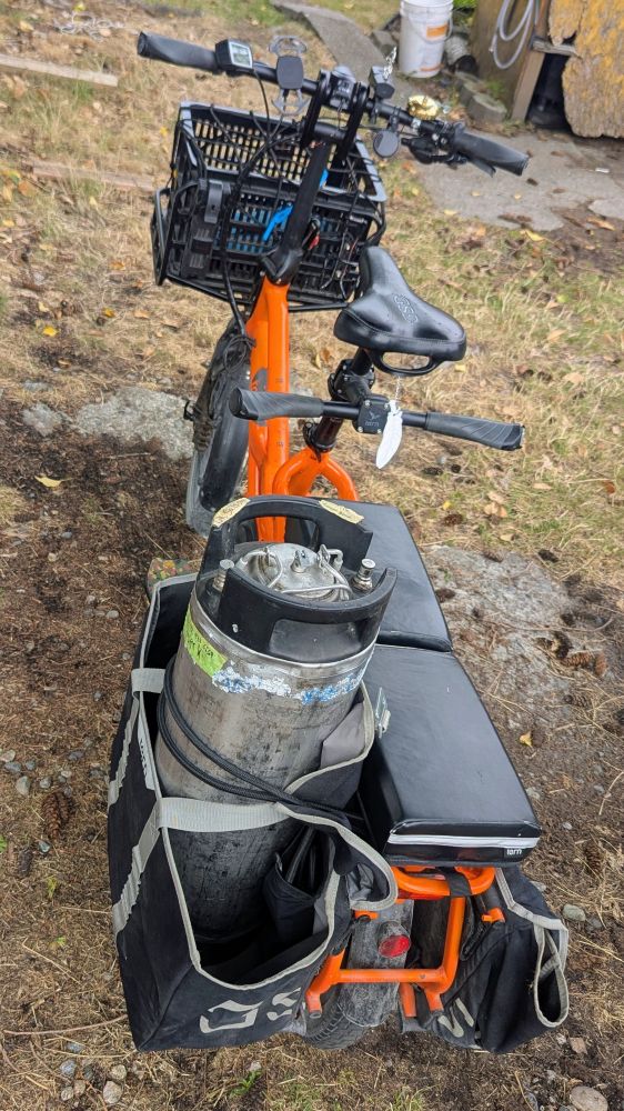 Orange cargobike with a keg of beer strapped upright into the rear left bag