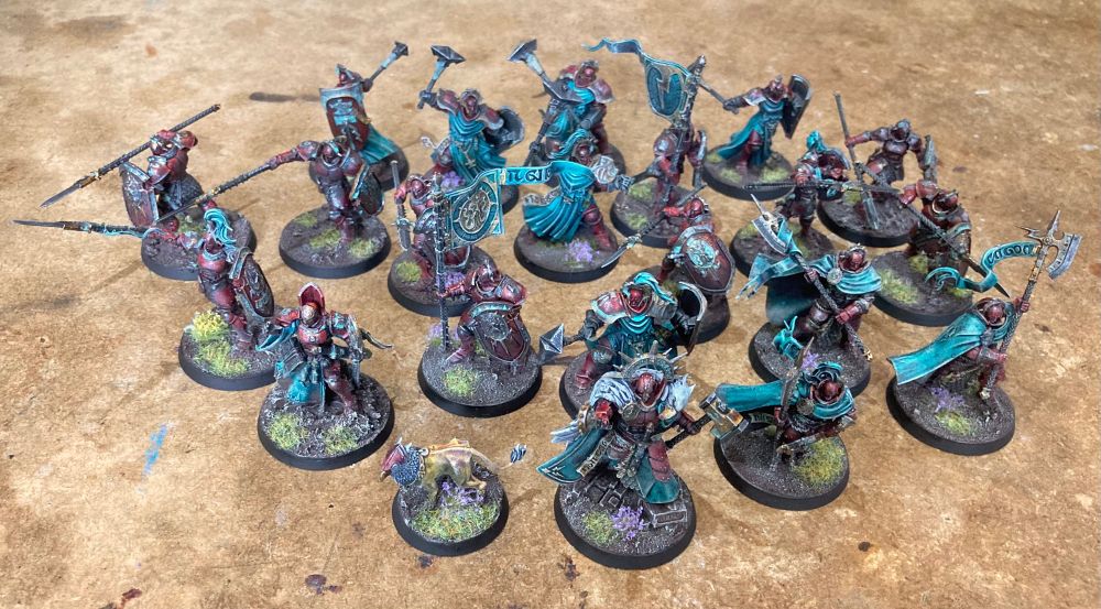 Selection of Stormcast Eternal infantry. They have dark red armour with worn paint and patina in the metal, as well as teal cloaks.