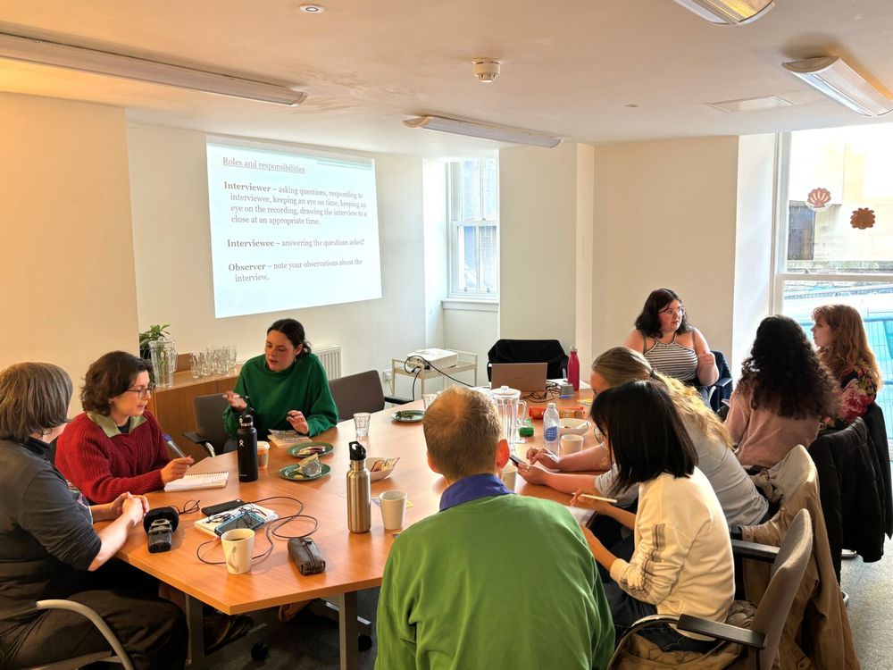 A group of people gathered round a table for a tailored training session provided by the Oral History Society. Interview recording equipment can be found on the table. 
