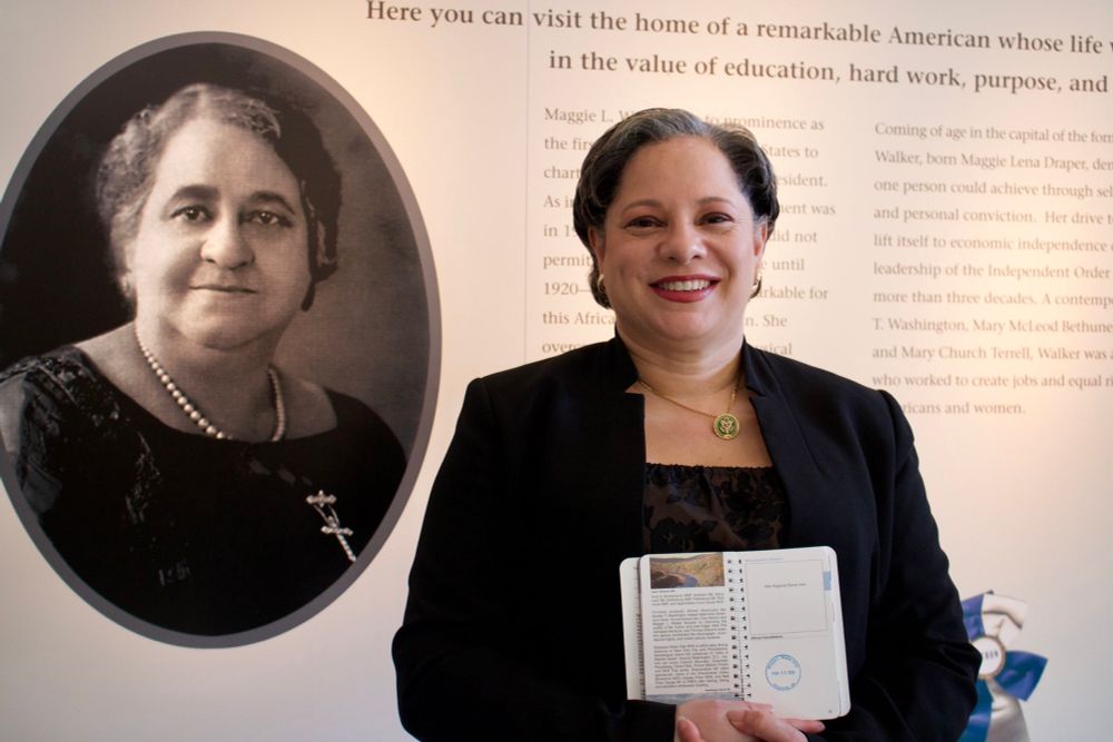 Photo of Rep. McClellan smiling in front of a display of Maggie L. Walker at the Maggie L. Walker National Historic Site.