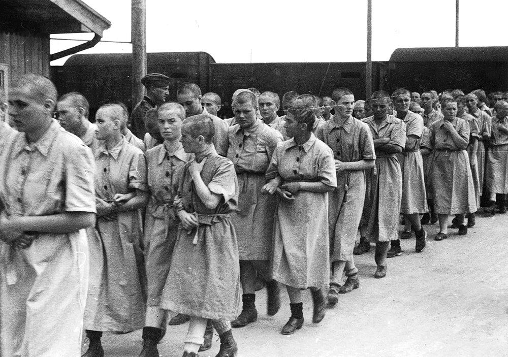 Photo of Hungarian Jewish women imprisoned in Auschwitz walking in a line monitored by soldiers.