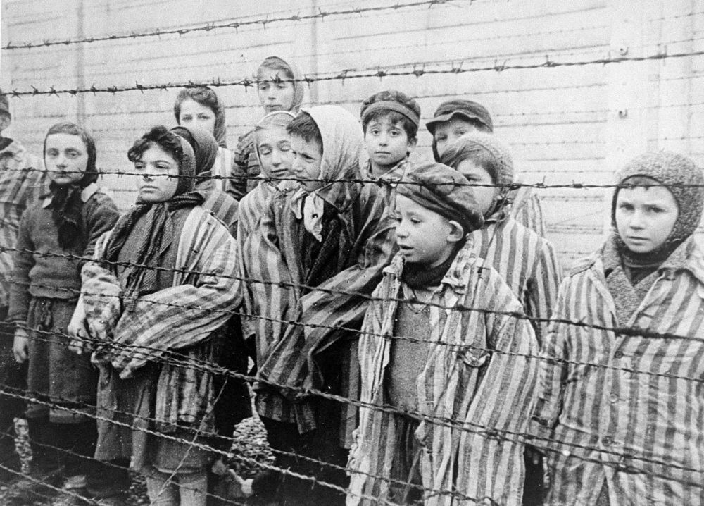 Photo of children imprisoned in Auschwitz lined up against a barbed wire fence.