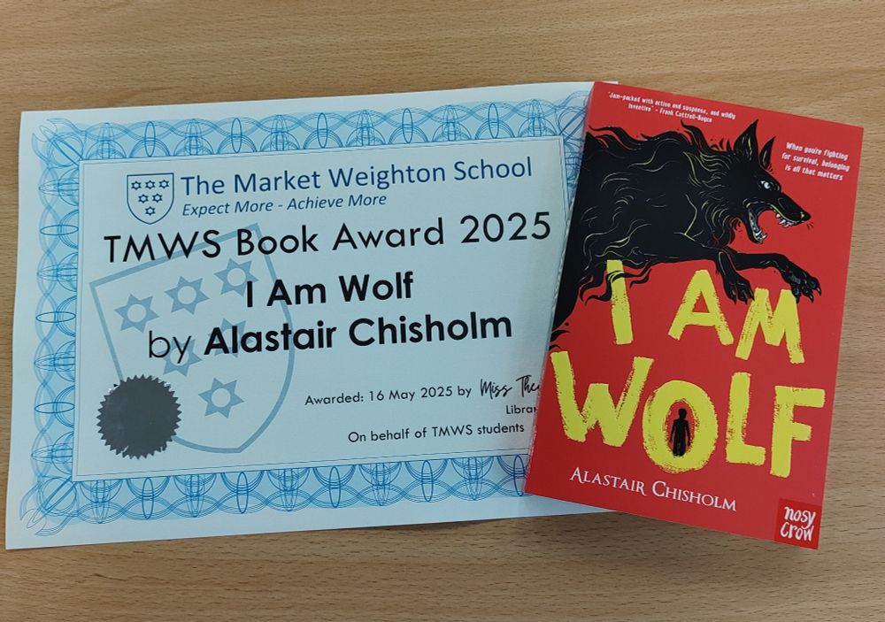 A certificate from The Market Weighton School for the TMWS Book Award 2025. Awarded to I Am Wolf by Alastair Chisholm. Awarded 16 May 2025 by Miss T (Librarian) on behalf of TMWS students. Next to it is a copy of the book itself.