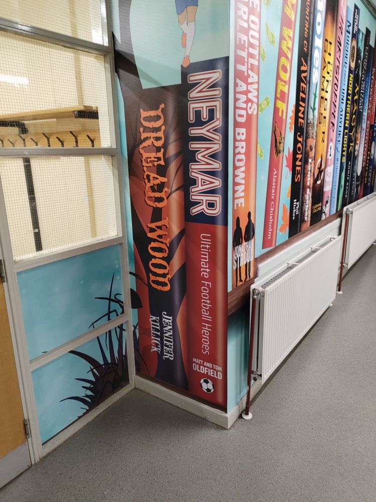 A pillar to the right of the library entrance is covered with artwork depicting two books: Dread Wood by Jennifer Killick and Neymar by Matt and Tom Oldfield.