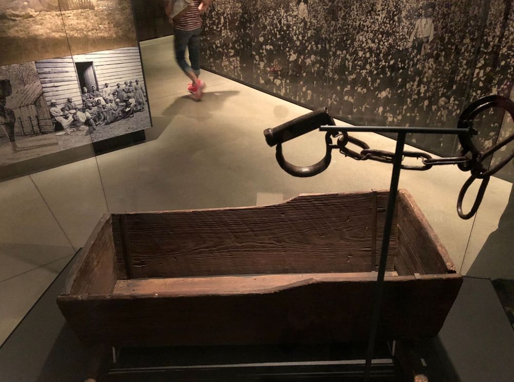 A small wooden crib in a display case with iron shackles suspended over it at the National Museum of African American History and Culture. 