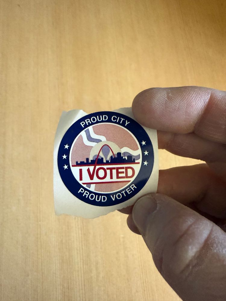 A hand holds an “I voted” sticker from the City of St. Louis elections board. 