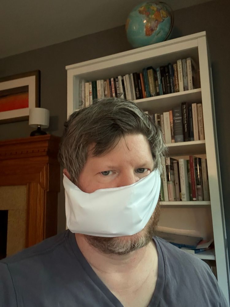 Man with a bandage wrapped around his head sitting in front of a bookshelf. 