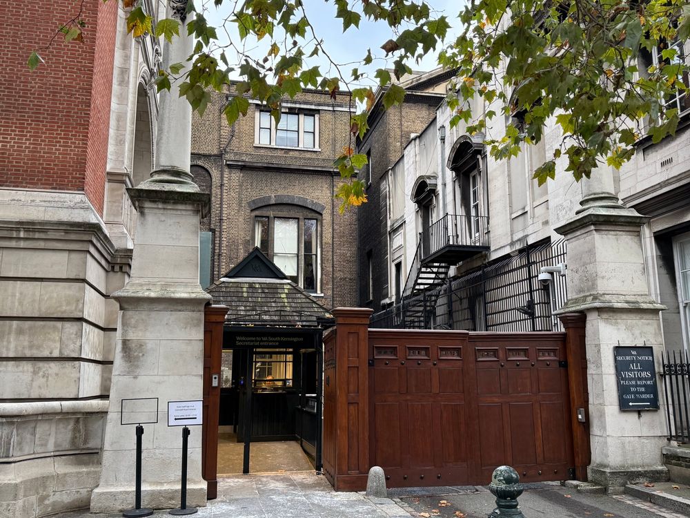 A wooden gate in front of brick buildings at the staff entrance to the Victoria and Albert Museum in London. 