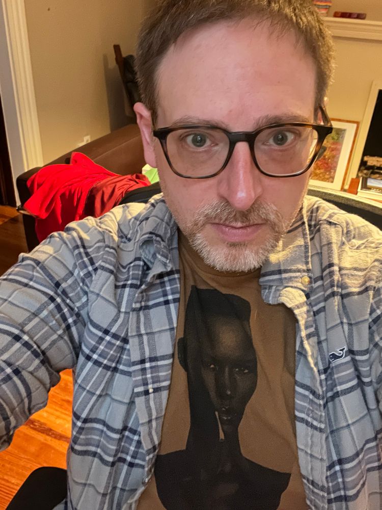 A middle-aged gay man wears a t-shirt featuring the iconic Grace Jones with cigarette hanging from her mouth from the cover of her 1981 album Nightclubbing.