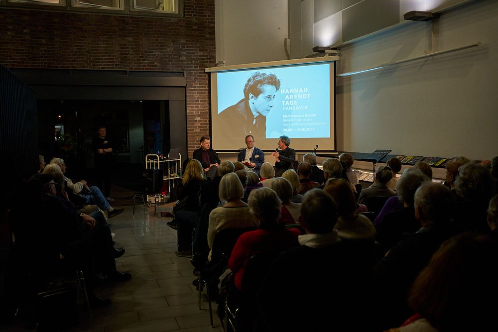 Totale des Podiums in der hannäverschen Stadtbibliothek - von rechts nach inks: Arendt-Biograf und Herausgeber Thomas Meyer, Tom Becker und ich. Publikum in Sitzreihen von hinten von fotografiert; ein Bild Arendts auf eine Leinwand projiziert.