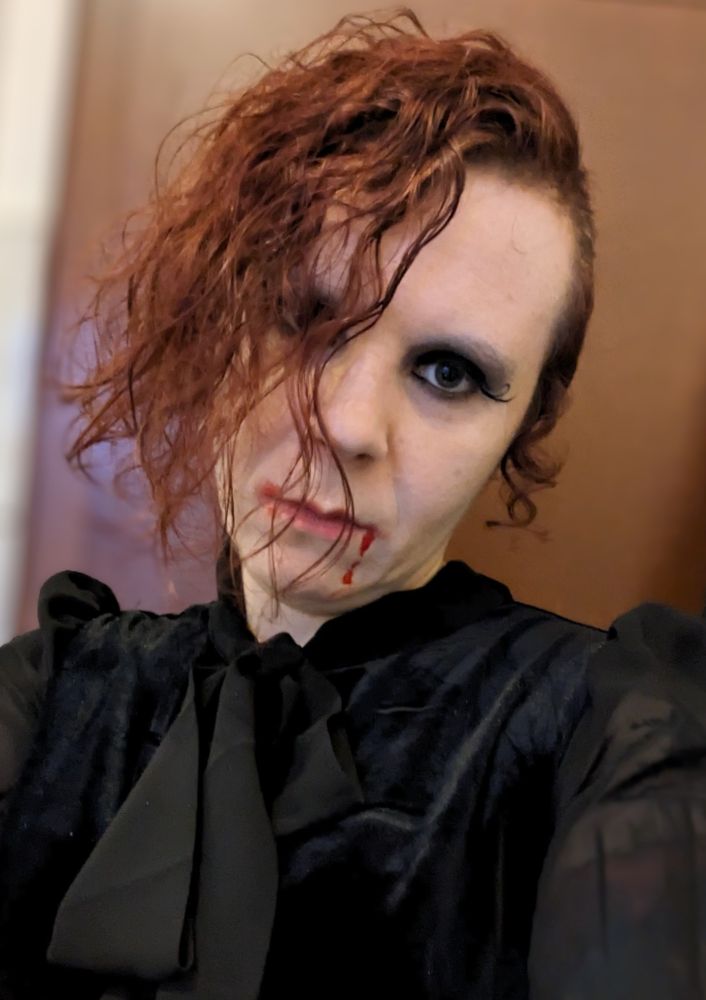 Selfie; strähniger Sidecut, dunkles Make-up, Blut fließt den Mund herab, schwarze Kleid