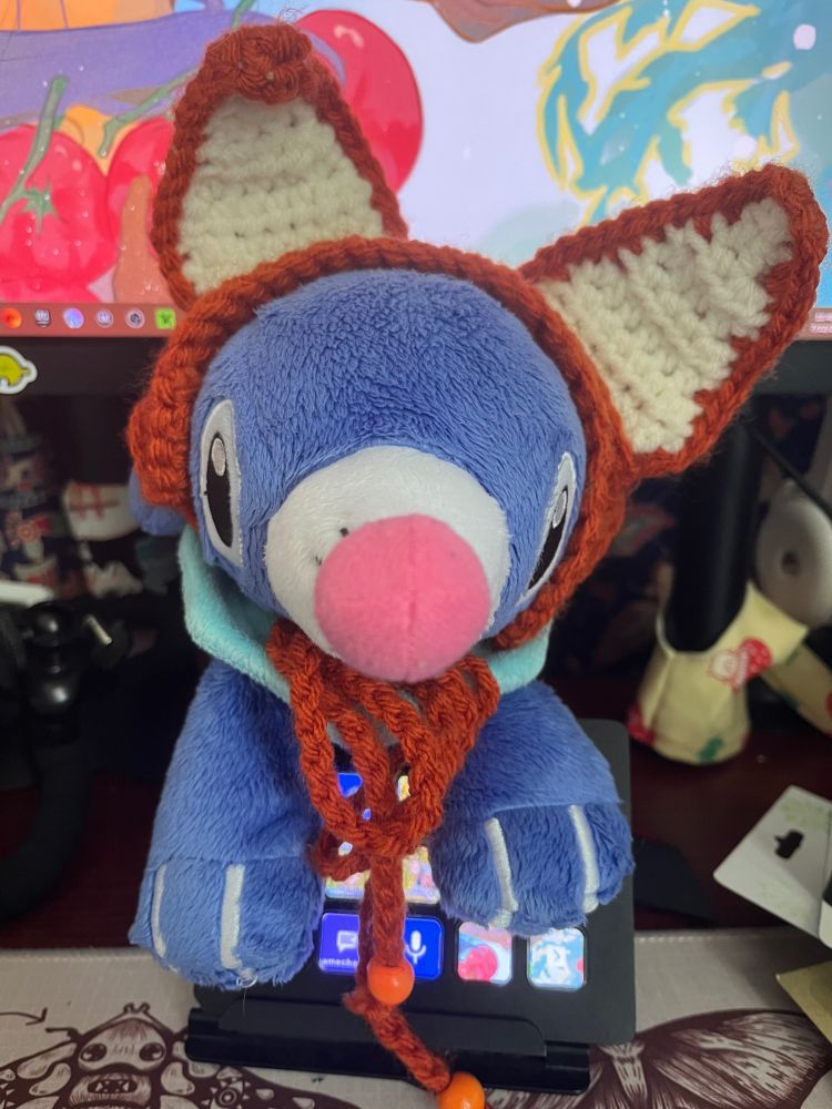 Popplio plush with crochet fox ears on him. He’s sitting on my stream deck. 