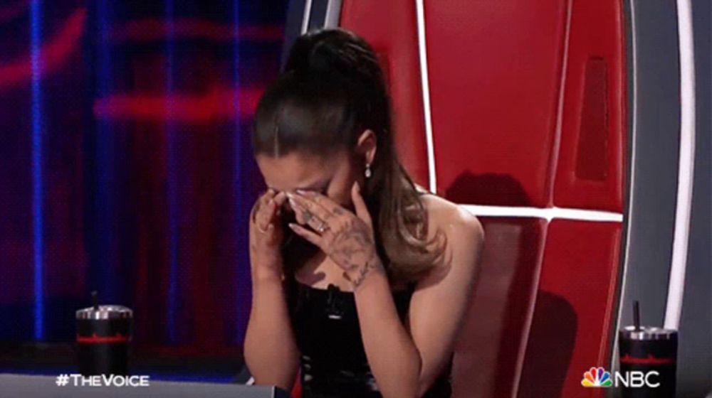 a woman is covering her face with her hands while sitting in a chair on the voice