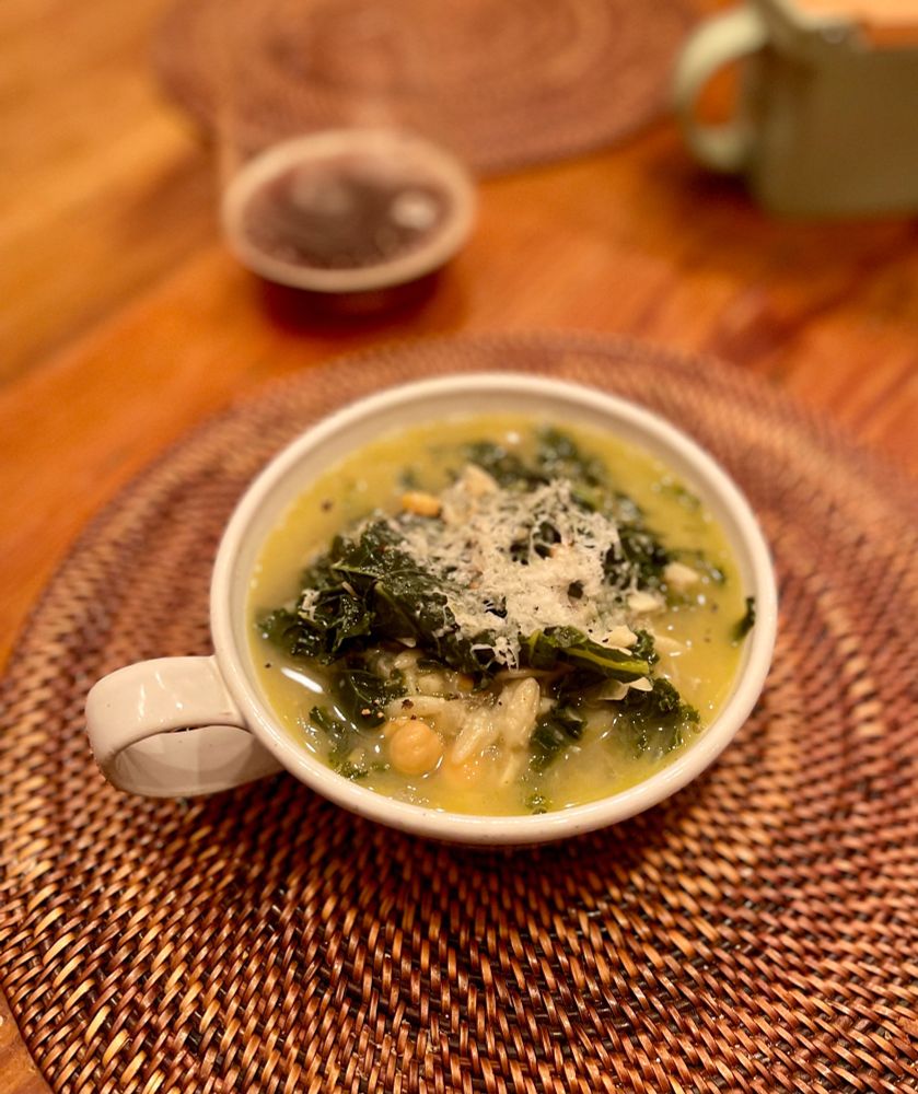 Soup bowl with beige colored soup, kale and cheese can be seen.