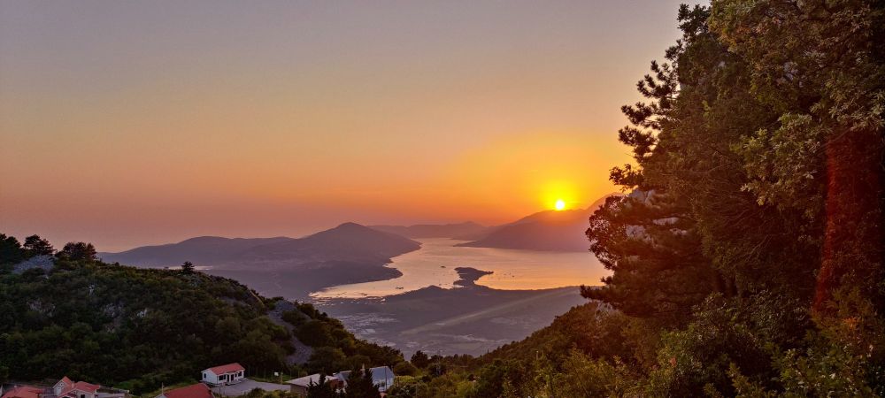 trees to the left sun shining up from a mountain little village in bottom left corner