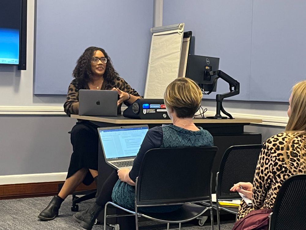 Speaker seated behind a desk, in front of an audience