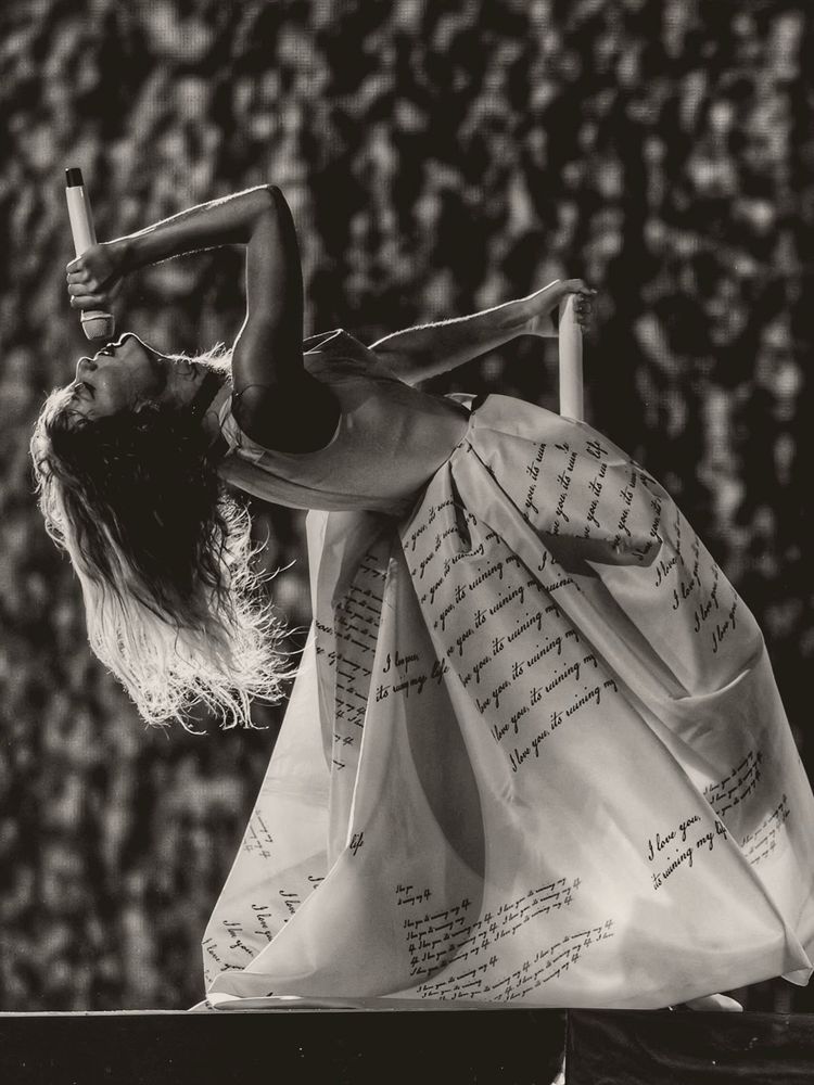 A black and white photograph from Taylor Swift wearing a long white dress while singing into a microphone 