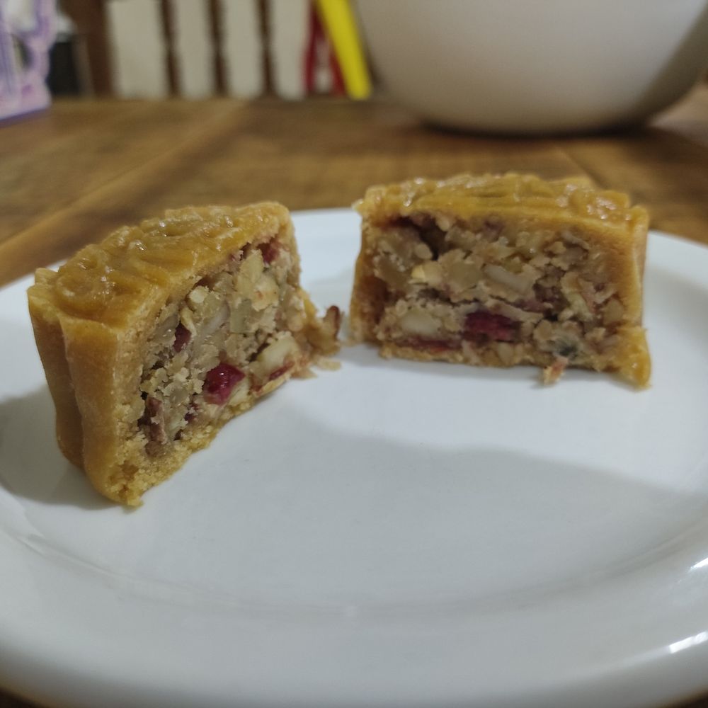 A mooncake on a white plate. The mooncake is split in half, revealing the mixed nut filling.