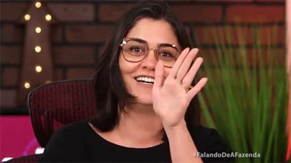 a woman wearing glasses is sitting in a chair waving her hand .