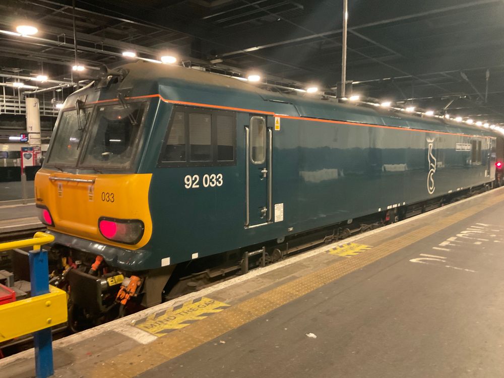 A train, which is mainly blue with a yellow front and red lights is waiting at a platform. 