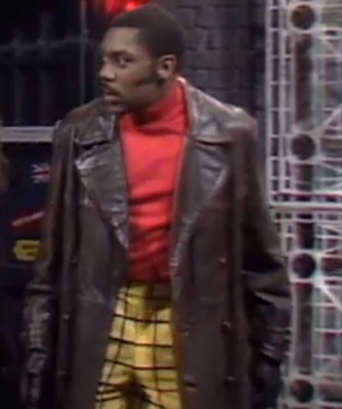Lenny Henry as the Doctor in a long, wangy collared, brown leather jacket and Rupert the Bear trousers.