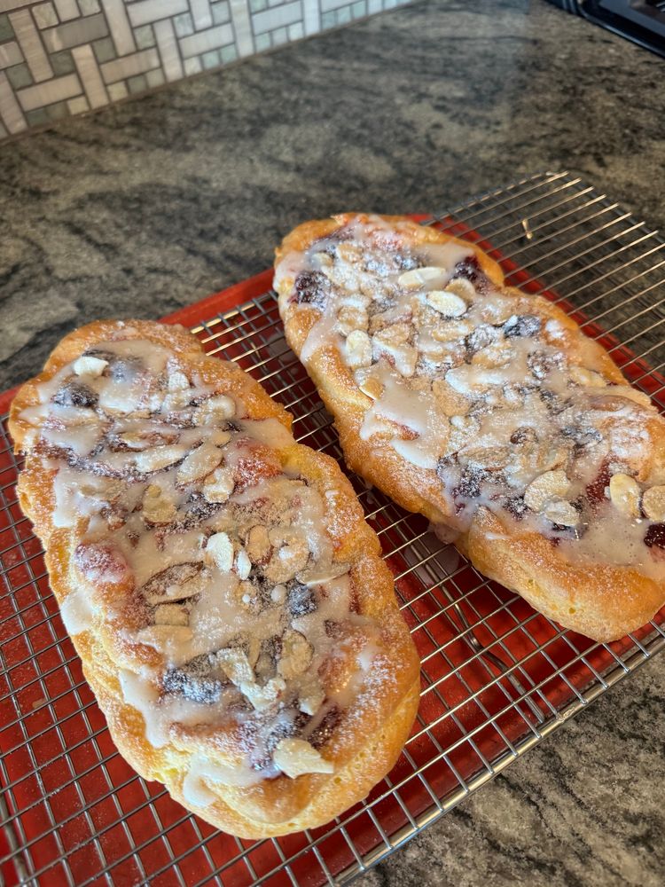Two somewhat rectangular pastries made with a biscuit layer, a layer of almond choux pastry and topped with jam, almonds and glaze.