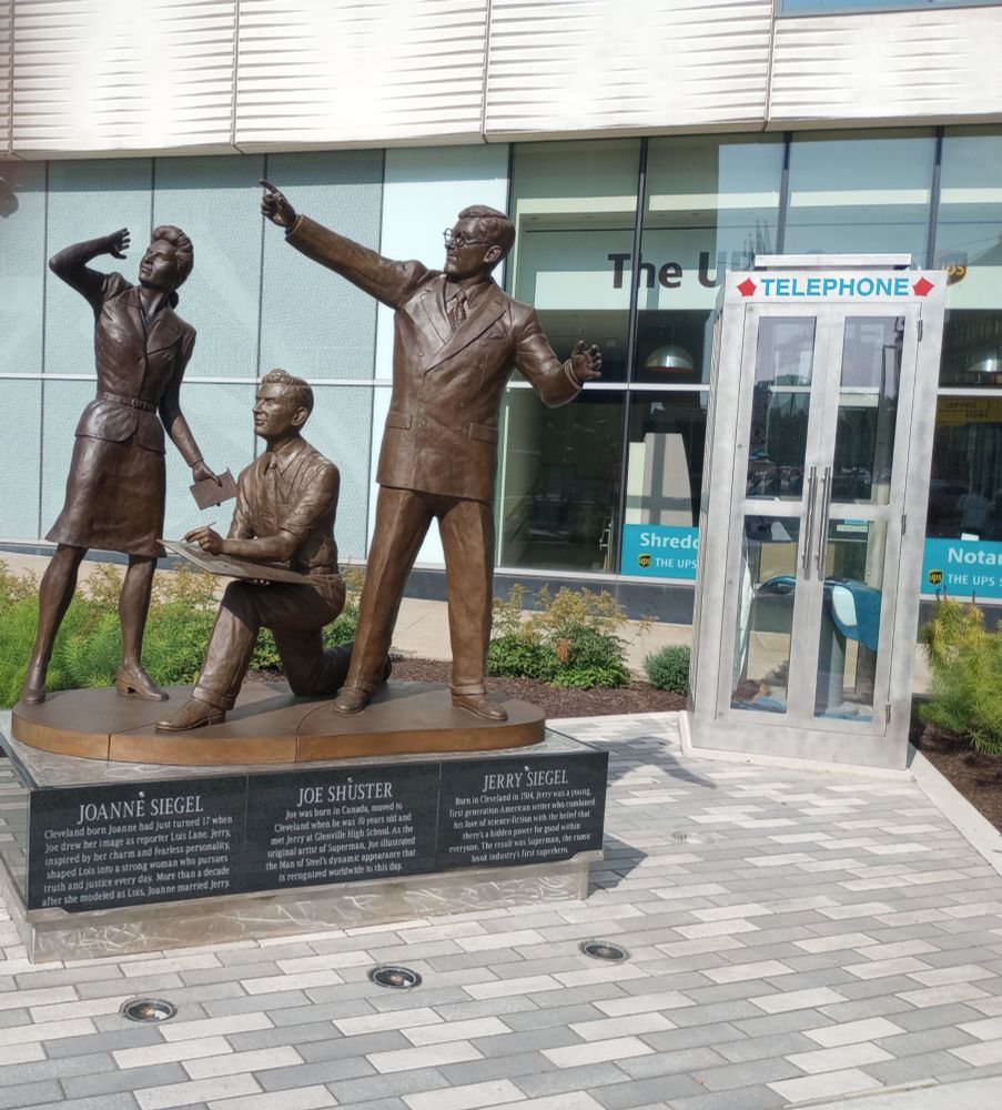 Statue of Joanne Siegel, Joe Shuster and Jerry Siegel in downtown Cleveland, looking at the statue of Superman, with the phone booth Clark Kent used to make his transformation behind them