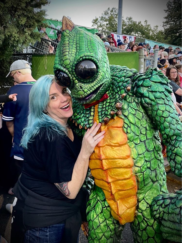 A blue haired woman excitedly embracing a man in a large Sleestak costume. 