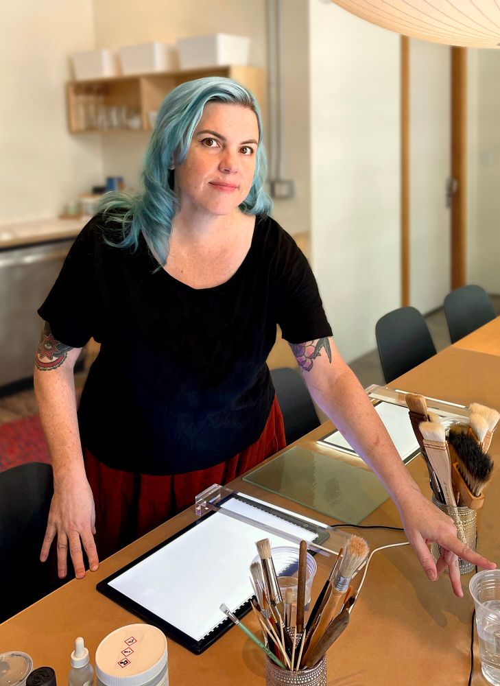 Me, Valerie Fairlight, standing over a table with light pads and brushes preparing to teach my first class. 