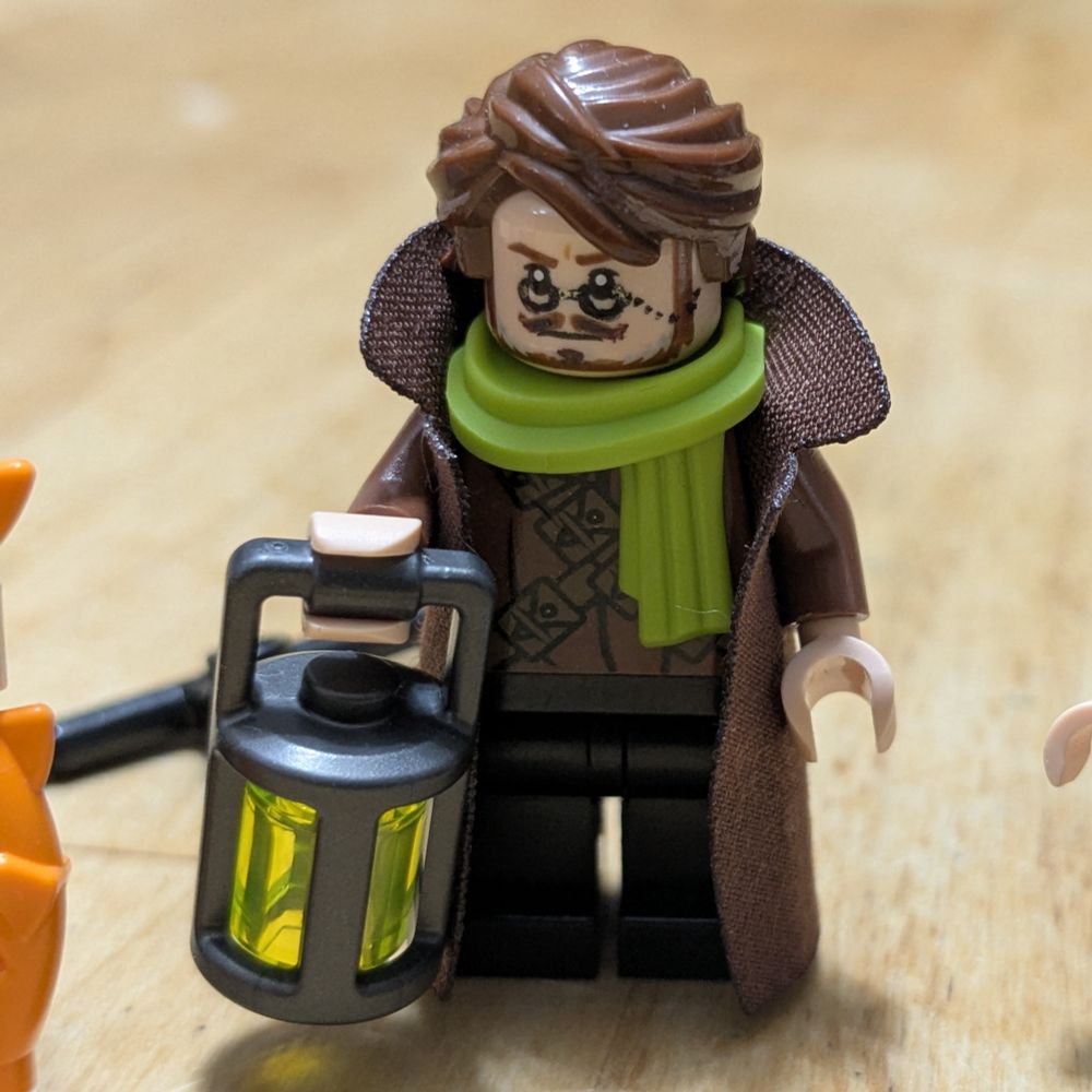 A Lego man wearing a brown overcoat, a green scarf, and holding a lantern