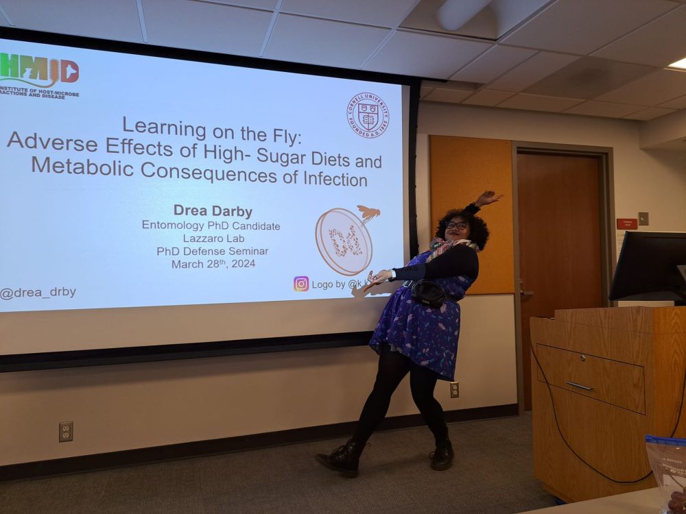 Dr. Drea Darby posing in front of her title slide of her dissertation titled "Learning on the Fly: Adverse Effects of High-Sugar Diets and Metabolic Consequences of Infection".