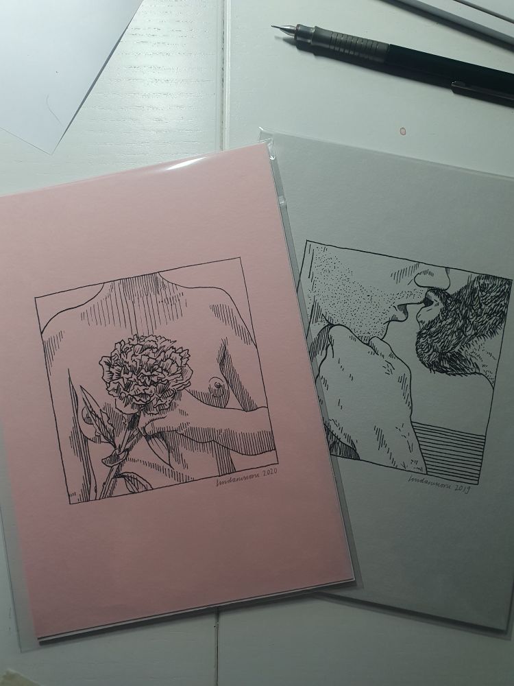 Twee prints op een bureau. Een roze papier met een illustratie van een naakt bovenlijf dat een bloem voor de borsten houdt. Een grijs papier met twee zoenende mannen