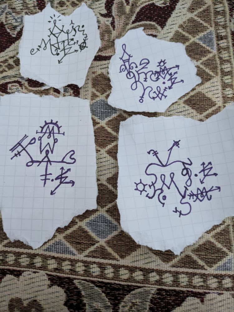 sigils on 4 pieces of torn paper ontop of a small patterned mat