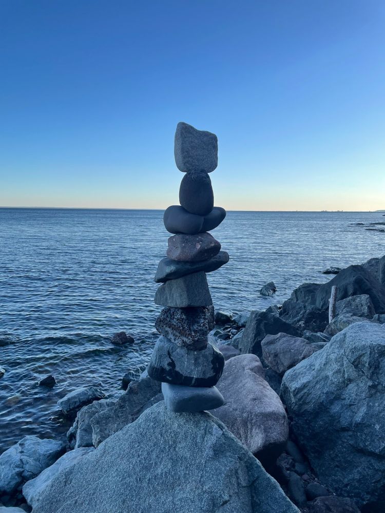Nine stones from Lake Superior piled on to of a boulder at dusk. The horizon is in the background and the water is calm.