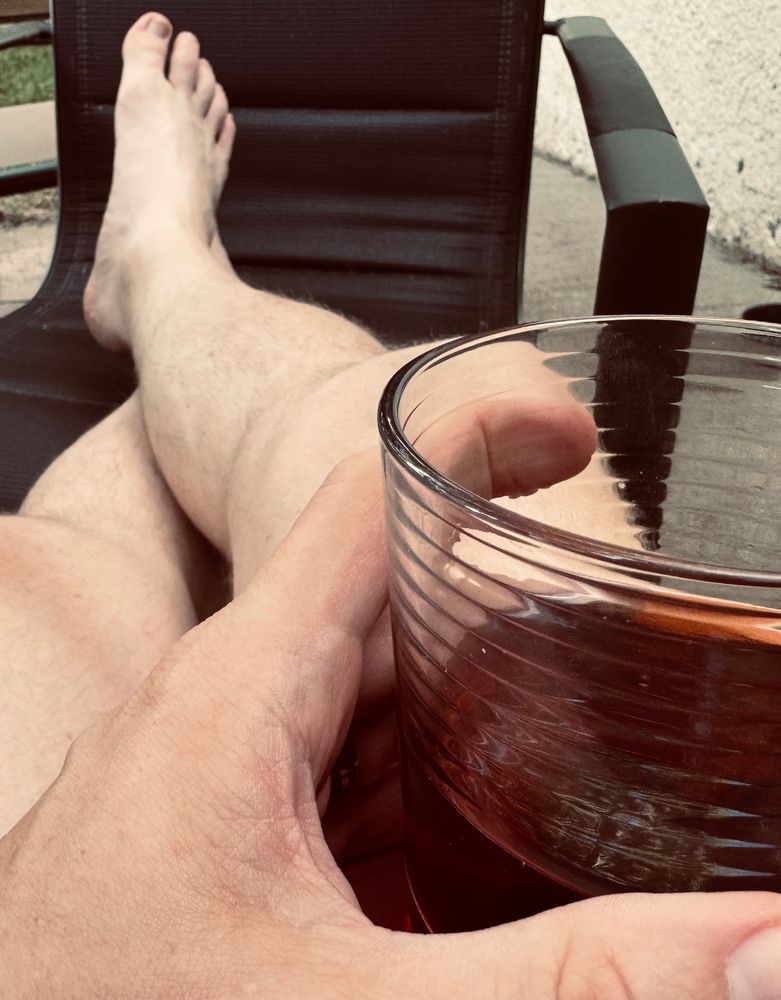 Legs crossed with feet up on a lawn chair. A hand holds an alcoholic beverage. 