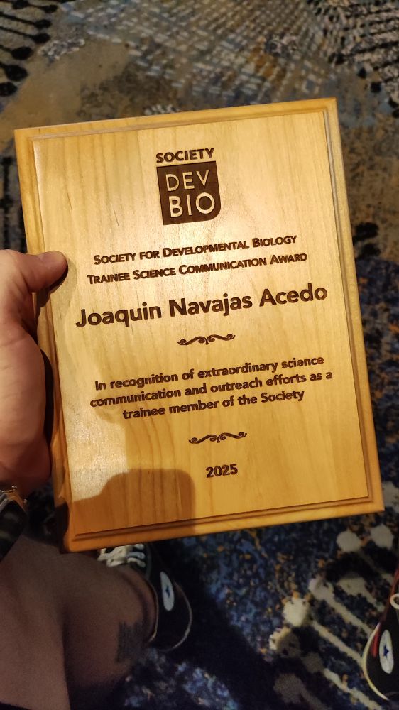 A plate made out of wood, with de society for dev bio logo, 2025 Trainee Science Communication Award, my name, and "In recognition of extraordinary science communication and outreach efforts as a trainee member of the Society"