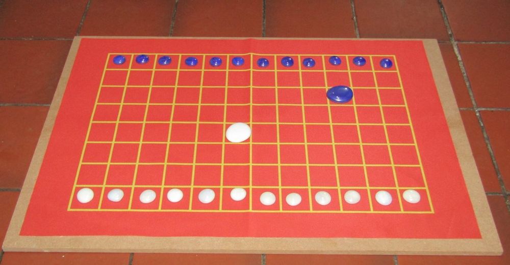 Blue and white playing counters are set up in their starting positions to play a startegy game called Aquila on a red 12x8 board of squares.  