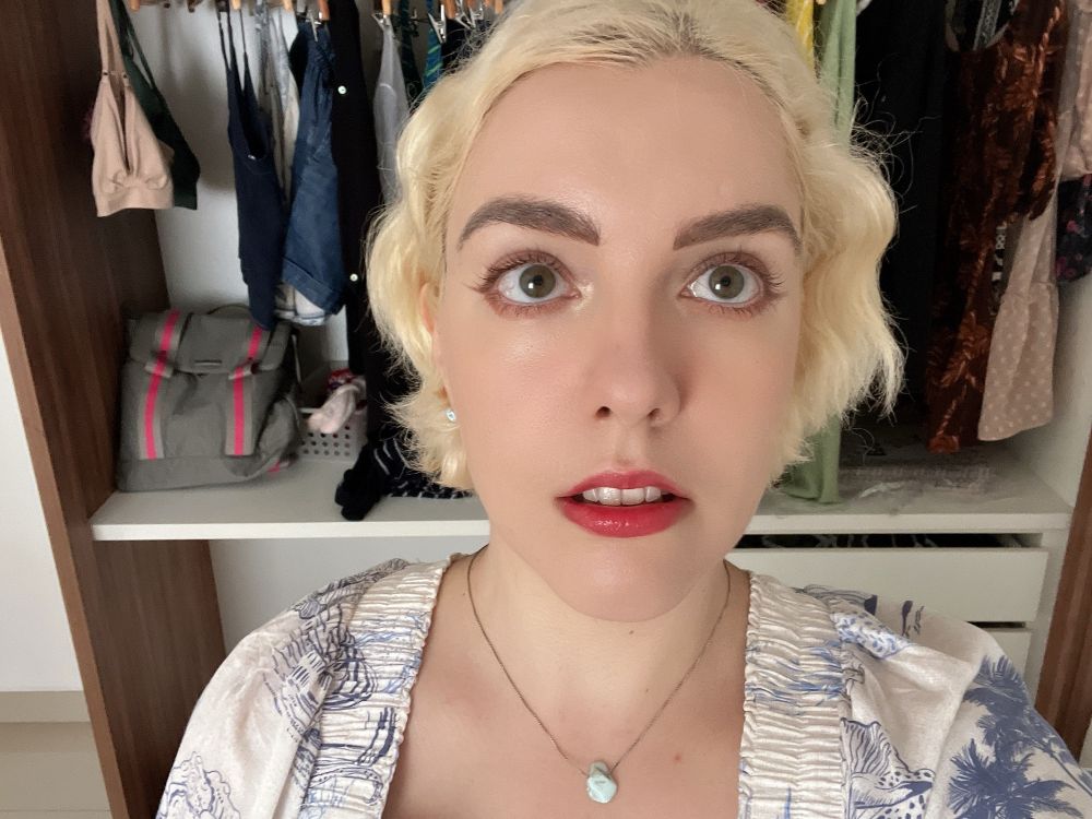 me with my short wavy platinum blonde hair and a full face of makeup, doing an expresionless “doll face” at the camera that shows my top front teeth 